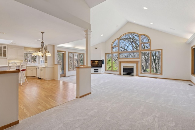 unfurnished living room featuring a fireplace with flush hearth, light carpet, lofted ceiling, a notable chandelier, and recessed lighting