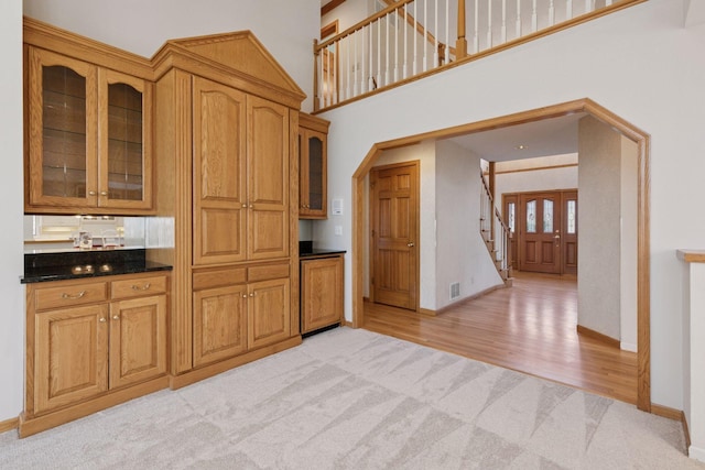 kitchen featuring dark countertops, visible vents, baseboards, glass insert cabinets, and light colored carpet