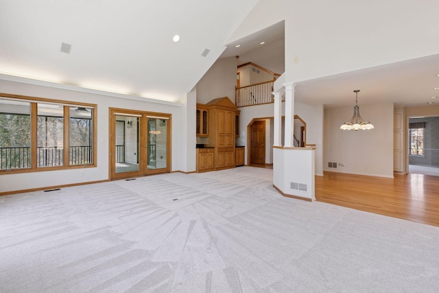 unfurnished living room featuring visible vents, high vaulted ceiling, light carpet, and an inviting chandelier