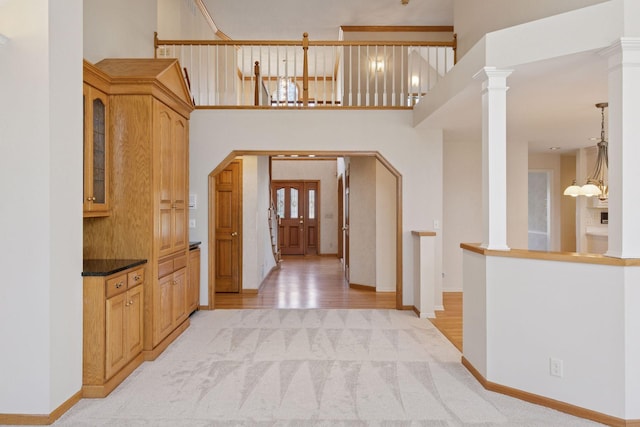 entrance foyer with arched walkways, baseboards, an inviting chandelier, ornate columns, and light colored carpet