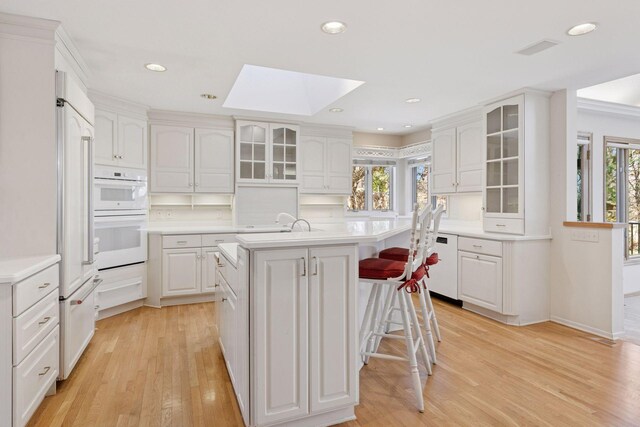 kitchen with light wood-type flooring, a skylight, white appliances, light countertops, and an island with sink