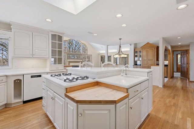 kitchen featuring white cabinetry, a kitchen island with sink, a sink, and white appliances