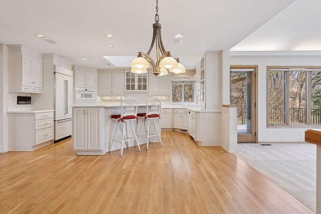 kitchen with light wood-style flooring, paneled built in refrigerator, glass insert cabinets, light countertops, and a breakfast bar area