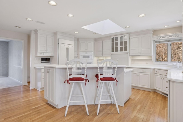 kitchen featuring paneled refrigerator, a breakfast bar, light wood-type flooring, a skylight, and white cabinetry