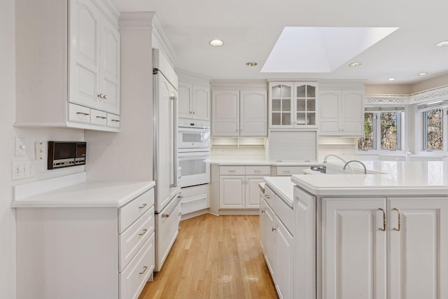 kitchen featuring a skylight, white double oven, white cabinets, and light wood-style flooring