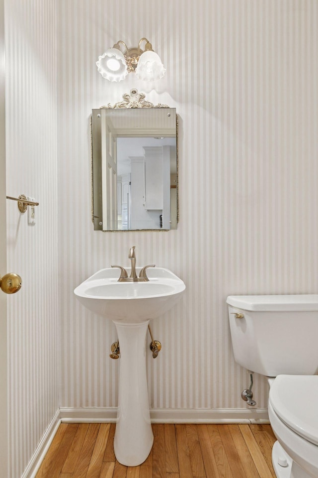 bathroom featuring toilet, wood finished floors, wallpapered walls, and baseboards