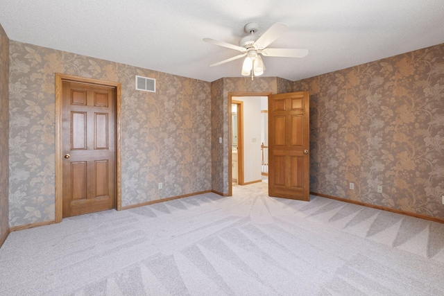 spare room with light colored carpet, baseboards, a ceiling fan, and visible vents