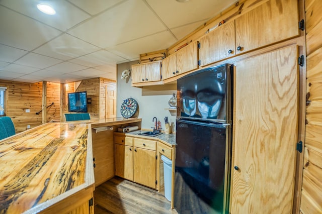 kitchen featuring sink, a paneled ceiling, black refrigerator, and wood walls