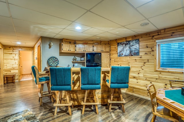 sitting room featuring bar area, hardwood / wood-style floors, a drop ceiling, and wooden walls