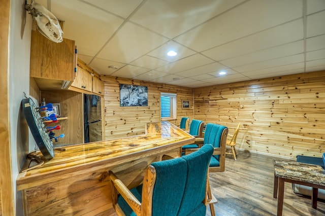 bar featuring a paneled ceiling, wood walls, black refrigerator, and light hardwood / wood-style floors