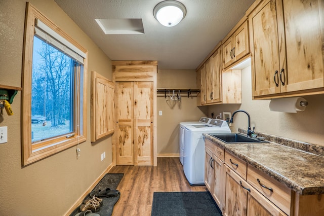 laundry area featuring washing machine and clothes dryer, sink, cabinets, light hardwood / wood-style flooring, and a textured ceiling