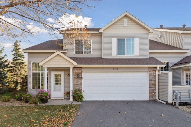 view of front of home featuring a garage, stone siding, roof with shingles, and driveway