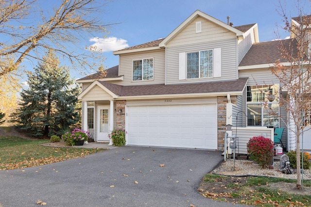 traditional-style home with stone siding, driveway, a shingled roof, and an attached garage