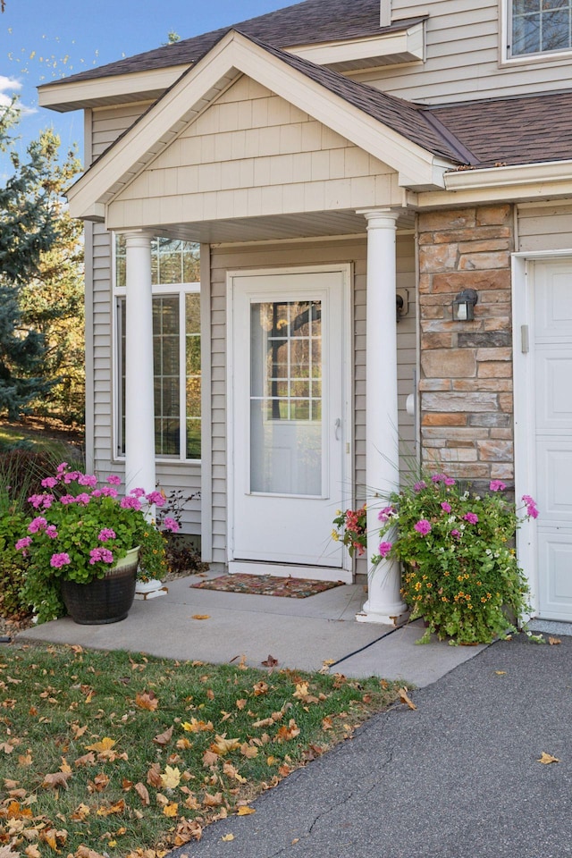 view of exterior entry featuring a garage, stone siding, and a shingled roof