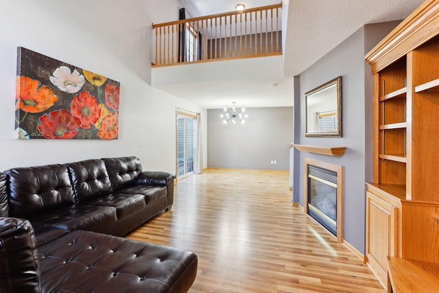 living area featuring baseboards, an inviting chandelier, a high ceiling, a glass covered fireplace, and light wood-type flooring