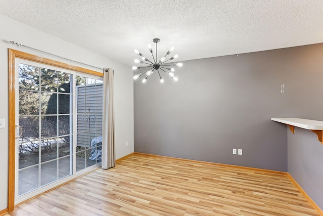 unfurnished dining area with a textured ceiling, wood finished floors, baseboards, and a chandelier