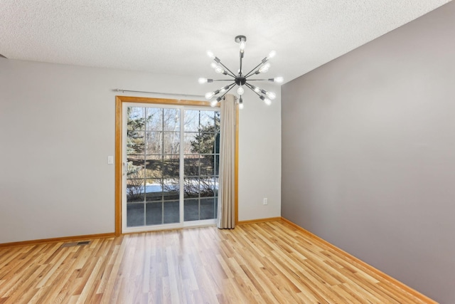 unfurnished dining area with visible vents, baseboards, an inviting chandelier, light wood-style flooring, and a textured ceiling