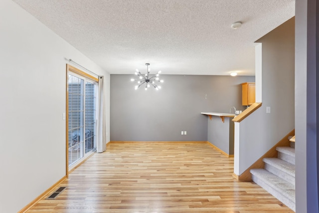 unfurnished dining area with light wood-type flooring, visible vents, a notable chandelier, and a textured ceiling