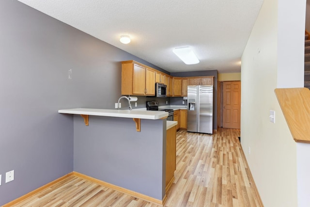 kitchen with light wood-style flooring, a peninsula, stainless steel appliances, and a kitchen bar