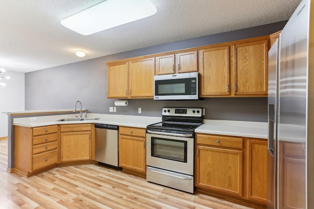 kitchen with a peninsula, a sink, stainless steel appliances, light countertops, and light wood-type flooring