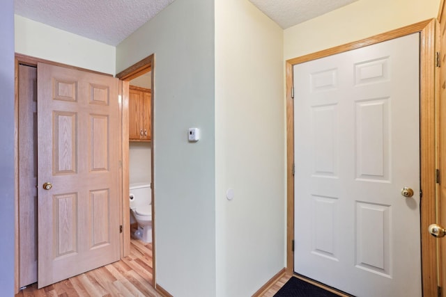 hallway featuring baseboards, a textured ceiling, and light wood finished floors