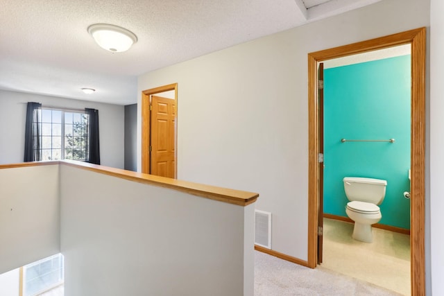 corridor featuring baseboards, visible vents, a textured ceiling, carpet flooring, and an upstairs landing