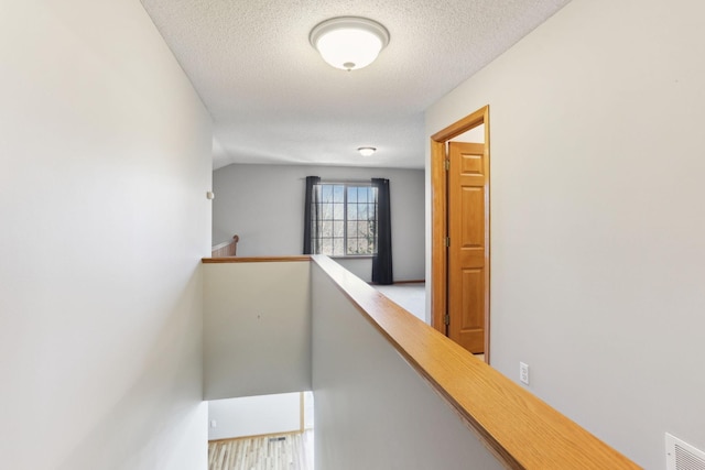 hall with visible vents, an upstairs landing, a textured ceiling, and lofted ceiling