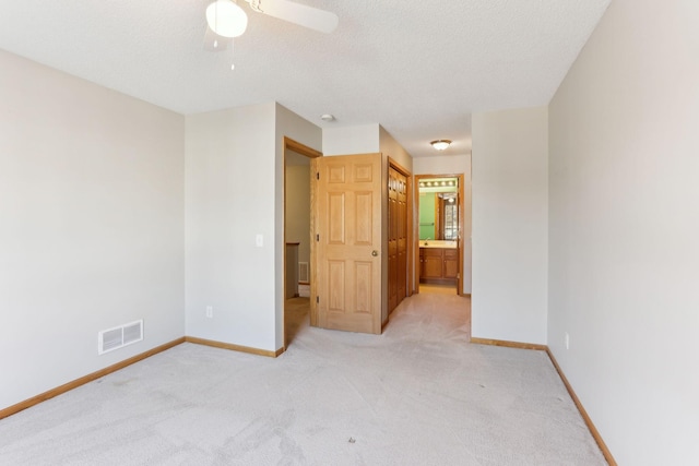 unfurnished bedroom with visible vents, a textured ceiling, ensuite bath, baseboards, and light colored carpet