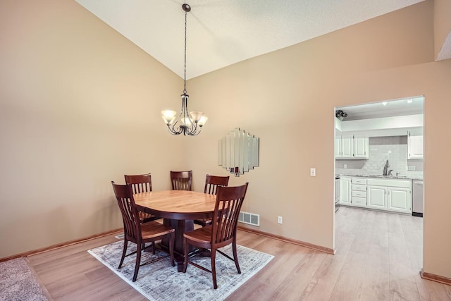 dining space featuring light wood-type flooring, a textured ceiling, a notable chandelier, high vaulted ceiling, and sink