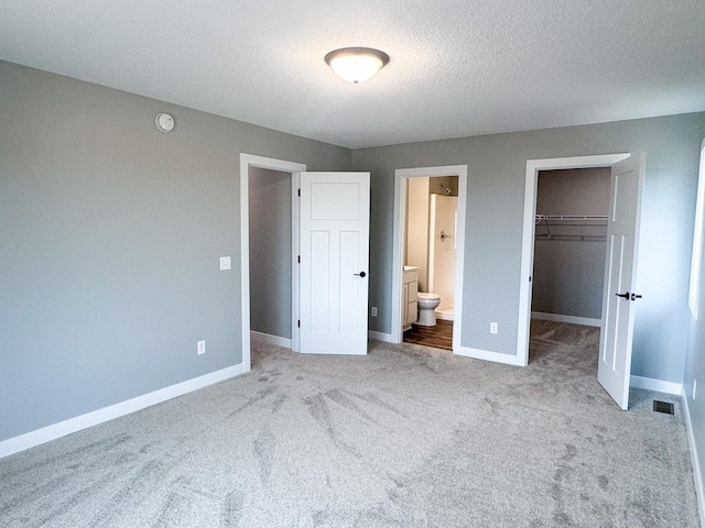 unfurnished bedroom featuring a closet, a walk in closet, ensuite bathroom, and light colored carpet