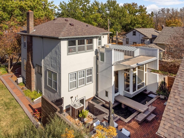 rear view of property with roof with shingles, a chimney, stucco siding, central AC unit, and fence