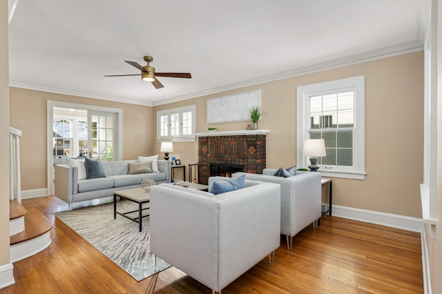 living room with a brick fireplace, crown molding, baseboards, and wood finished floors