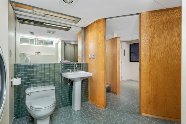 bathroom with a sink, tile walls, and toilet