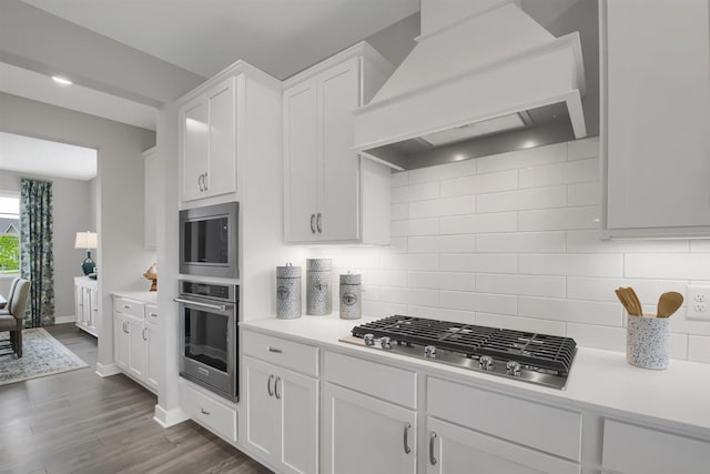 kitchen featuring dark hardwood / wood-style flooring, tasteful backsplash, premium range hood, stainless steel appliances, and white cabinetry