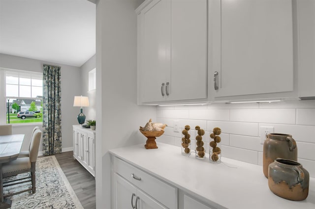 kitchen with wood-type flooring, backsplash, and white cabinetry