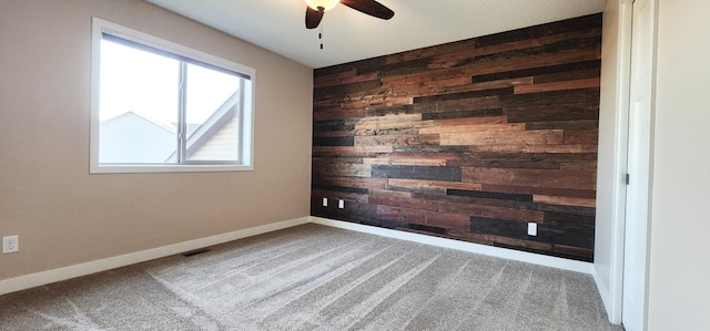 carpeted empty room featuring ceiling fan and wood walls