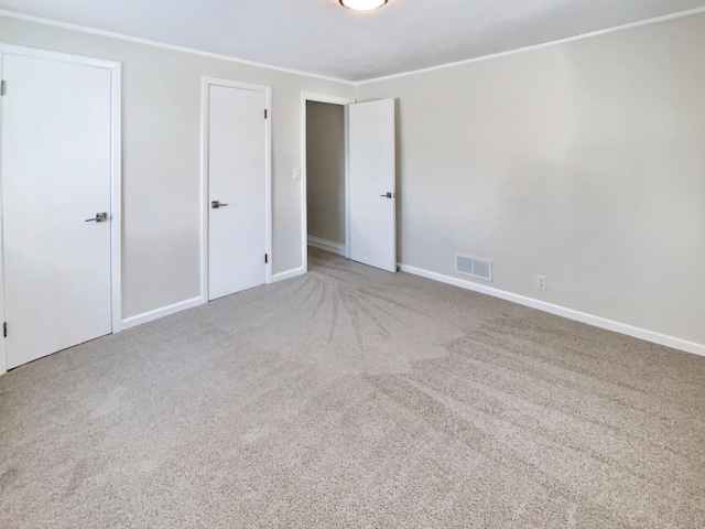 unfurnished bedroom with crown molding, carpet floors, visible vents, and baseboards