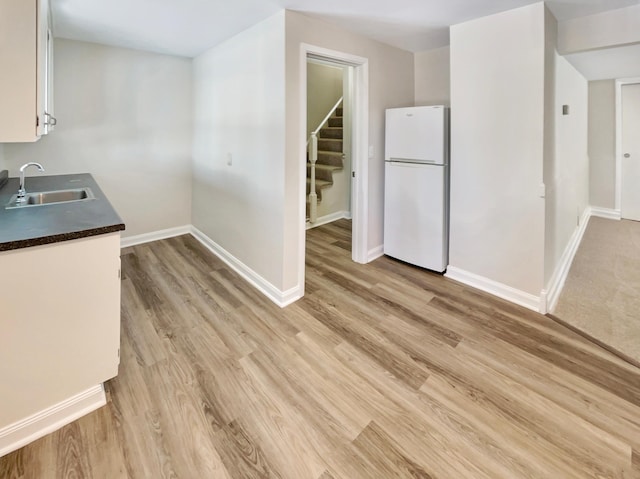 kitchen with dark countertops, freestanding refrigerator, light wood-type flooring, white cabinetry, and a sink