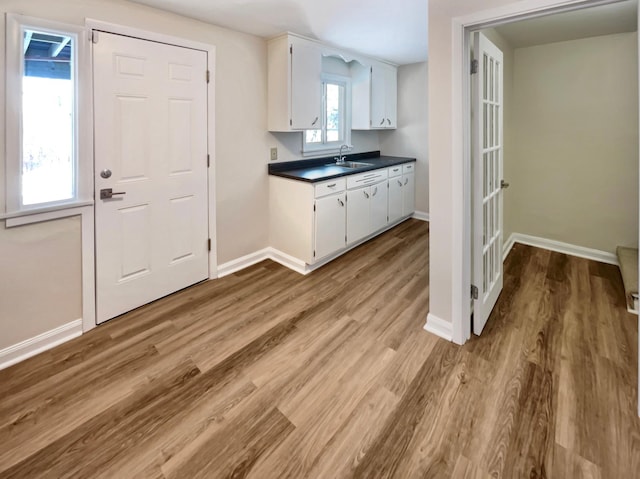 kitchen with dark countertops, white cabinetry, a sink, and light wood-style flooring