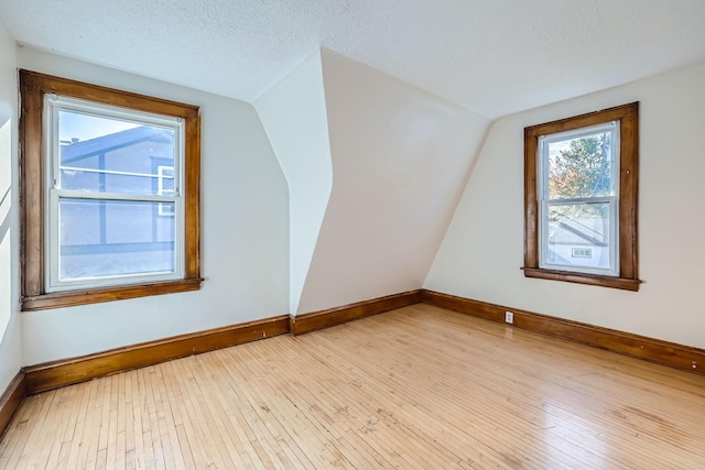 bonus room with light hardwood / wood-style floors, vaulted ceiling, and a textured ceiling