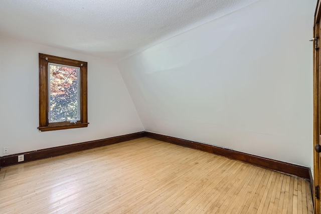 empty room with vaulted ceiling, a textured ceiling, and light wood-type flooring