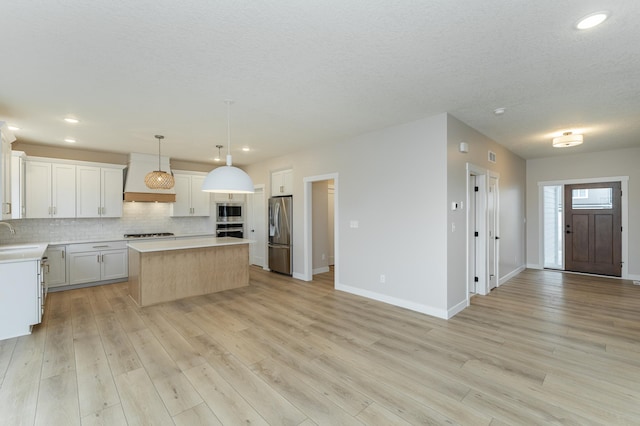 kitchen featuring light hardwood / wood-style flooring, appliances with stainless steel finishes, decorative light fixtures, a kitchen island, and white cabinetry