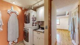 laundry room with cabinets, stacked washer and clothes dryer, track lighting, and light hardwood / wood-style floors