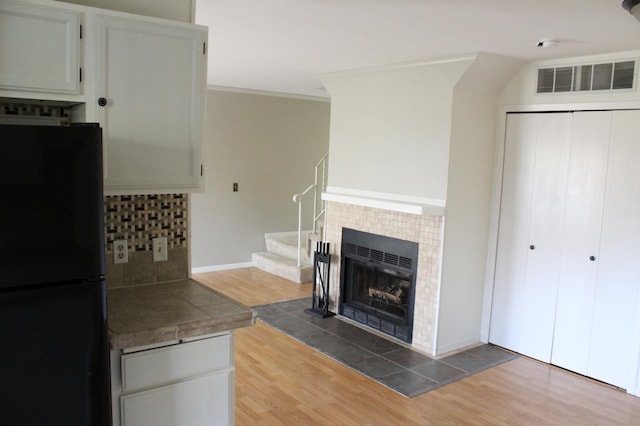 kitchen with white cabinets, tasteful backsplash, a tiled fireplace, hardwood / wood-style flooring, and black refrigerator