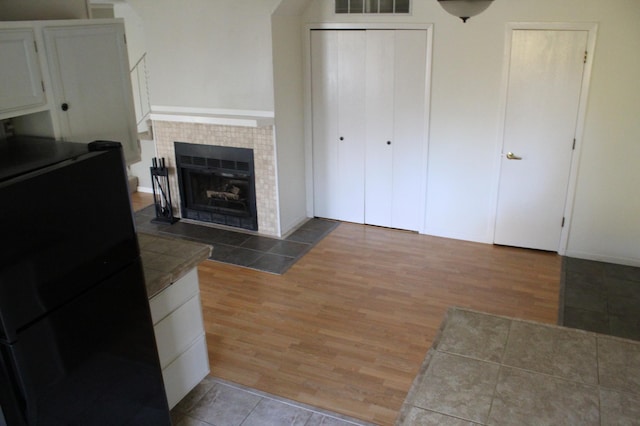 kitchen with tile countertops, light hardwood / wood-style flooring, white cabinets, and a tile fireplace