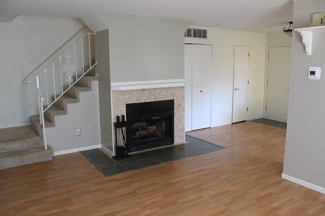 unfurnished living room with wood-type flooring and a tile fireplace