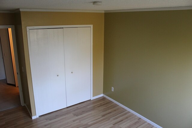 unfurnished bedroom with a closet, a textured ceiling, ornamental molding, and light hardwood / wood-style flooring