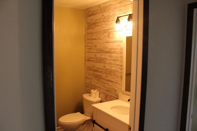 bathroom with vanity, wooden walls, and toilet