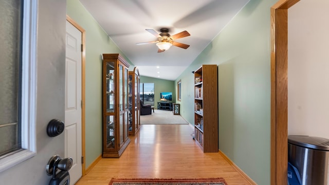 hall with light wood-style floors, baseboards, and vaulted ceiling