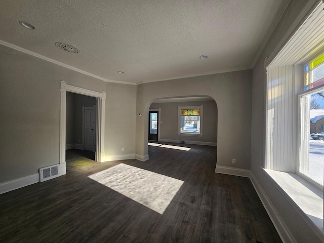 unfurnished room featuring visible vents, ornamental molding, a textured ceiling, arched walkways, and dark wood-style flooring